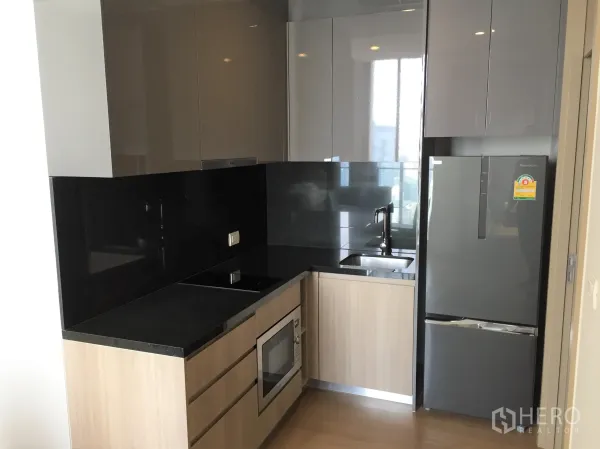 Condominium for rent in Pathum Wan, Bangkok - Compact modern kitchen with glossy cabinets, black backsplash and built-in appliances.