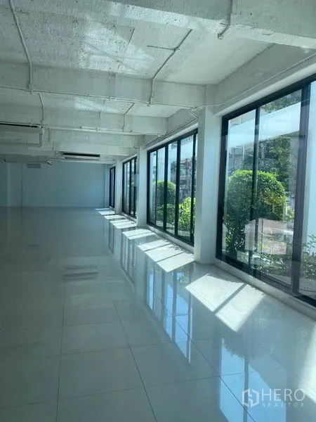Office Space for rent in Khlong Toei, Bangkok - Long open-plan office with large windows bringing in natural light and views of greenery outside.