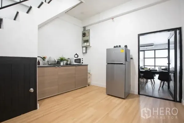 Townhouse for rent in Sathon, Bangkok - Functional kitchen under the stairs with ample cabinets, microwave, and stainless refrigerator.