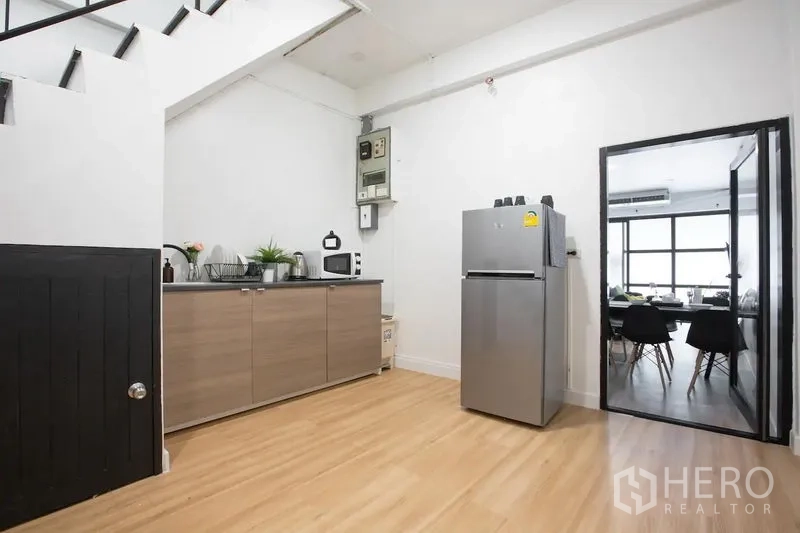 Townhouse for rent in Sathon, Bangkok - Functional kitchen under the stairs with ample cabinets, microwave, and stainless refrigerator.