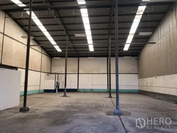 Warehouse for rent in Lat Krabang, Bangkok - Empty warehouse bay with tall pillars, metal roof, and suspended industrial lighting.