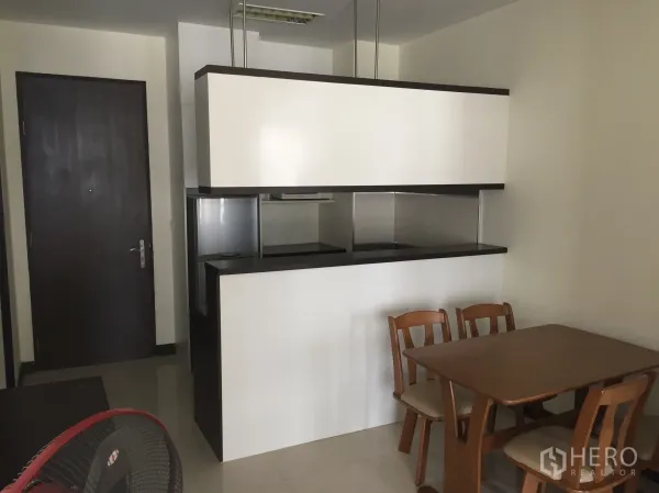 Condominium for rent in Khlong Toei, Bangkok - Dining area with wooden table beside a compact semi-open kitchen and entrance door.