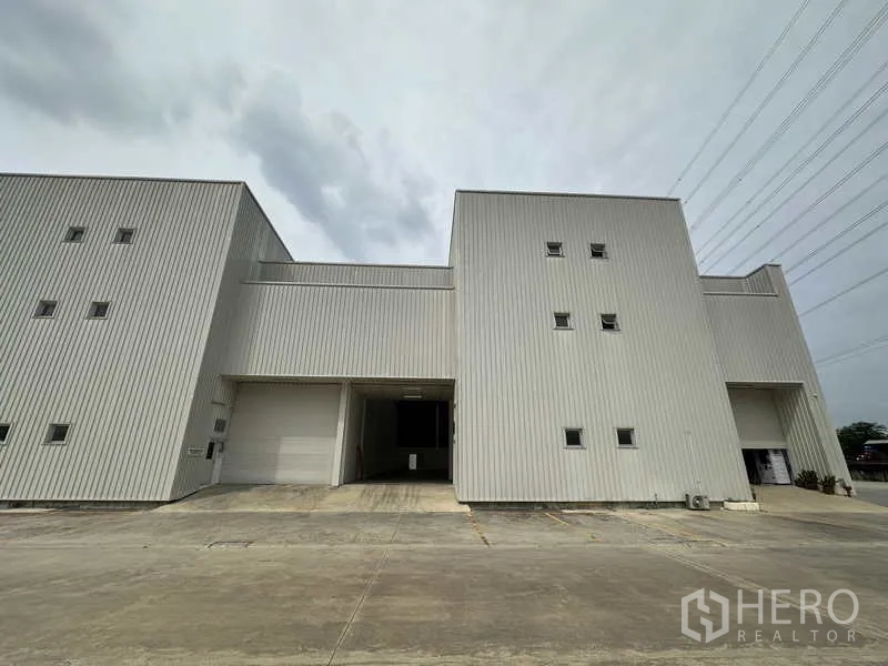 Factory for rent in Khlong Luang, Pathum Thani - Front elevation of steel-clad factory unit with large roller shutter and parking area.