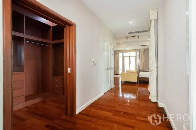 Detached House for rent in Watthana, Bangkok - Walk-in closet with custom wooden cabinetry leading toward a bedroom suite.