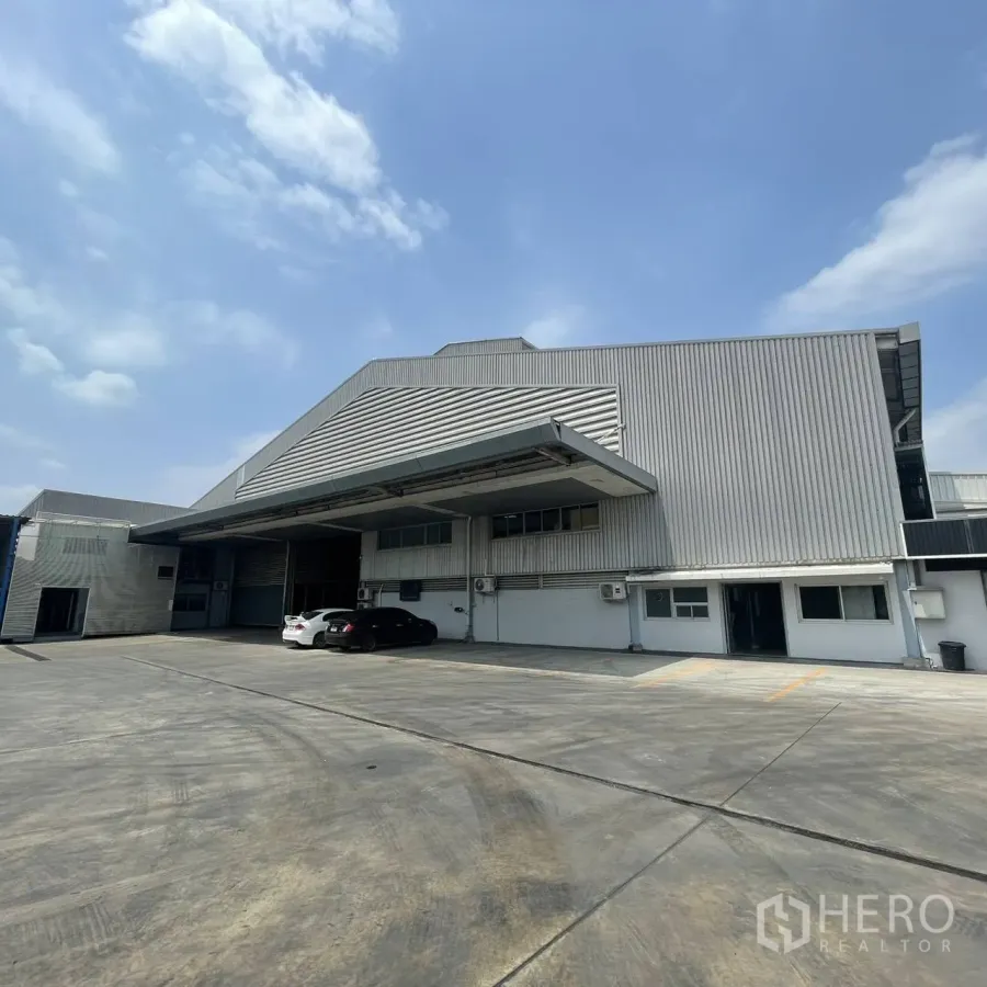 Factory for rent in Khlong Toei, Bangkok - Metal-clad factory exterior with large loading canopy and wide concrete yard under blue sky.