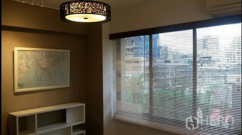 Condominium for rent in Khlong Toei, Bangkok - Bright room with large windows and blinds, city view, map artwork and shelving unit.
