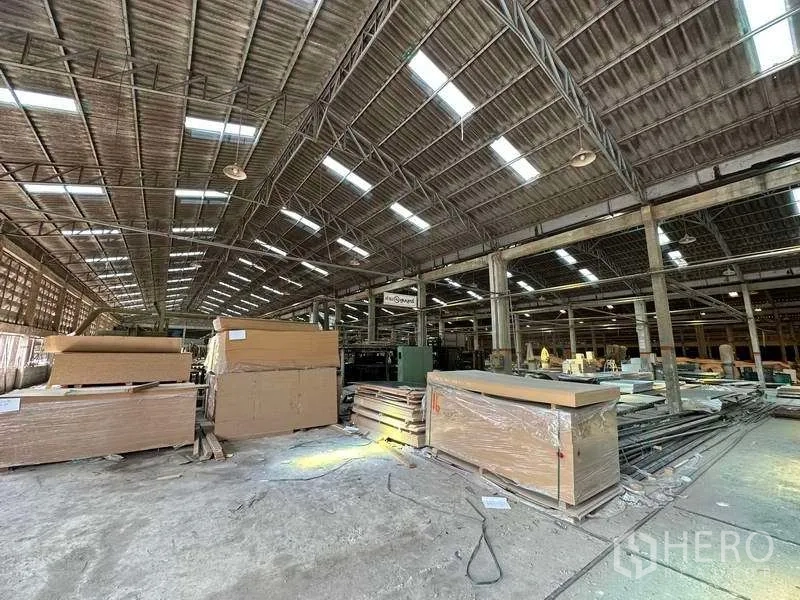 Factory for rent in Sai Noi, Nonthaburi - Factory interior with stacks of panels and a high clear-span roof with skylights and industrial lighting.