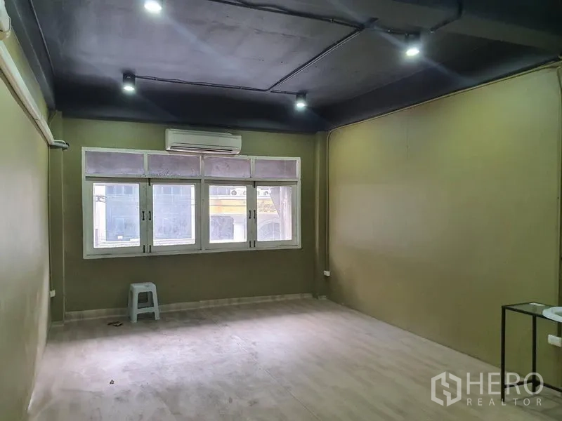 Shophouse for rent in Khlong Toei, Bangkok - Upper-floor open room with air conditioner, large windows, black ceiling with spotlights and light wood flooring.