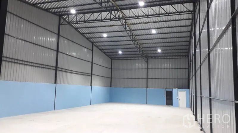 Warehouse for rent in Khlong Luang, Pathum Thani - Open warehouse space with high ceiling, large sliding doors and access to an internal room.