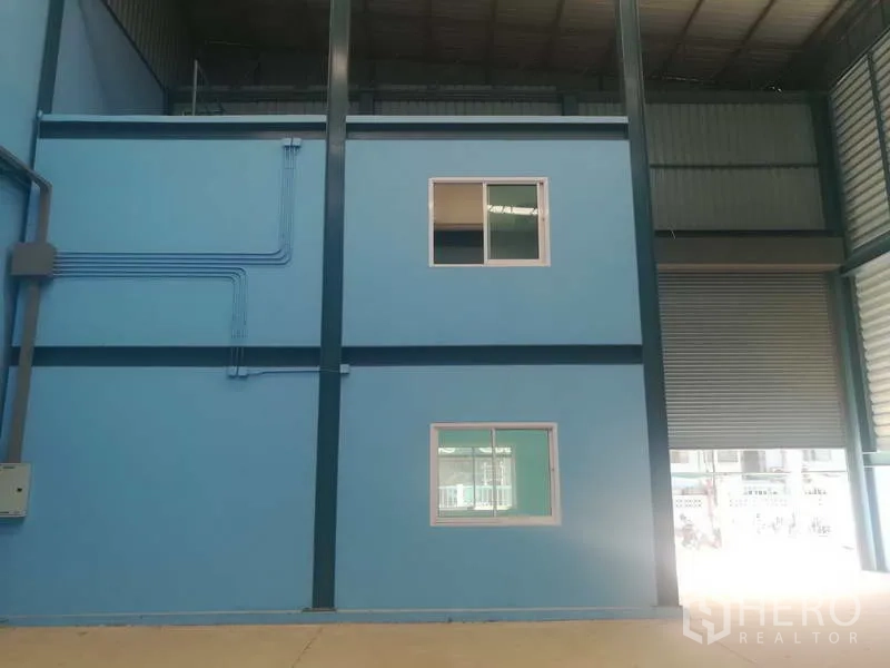 Factory for sale in Sai Noi, Nonthaburi - Two-storey internal office block within the warehouse, visible roller door and exposed conduits.