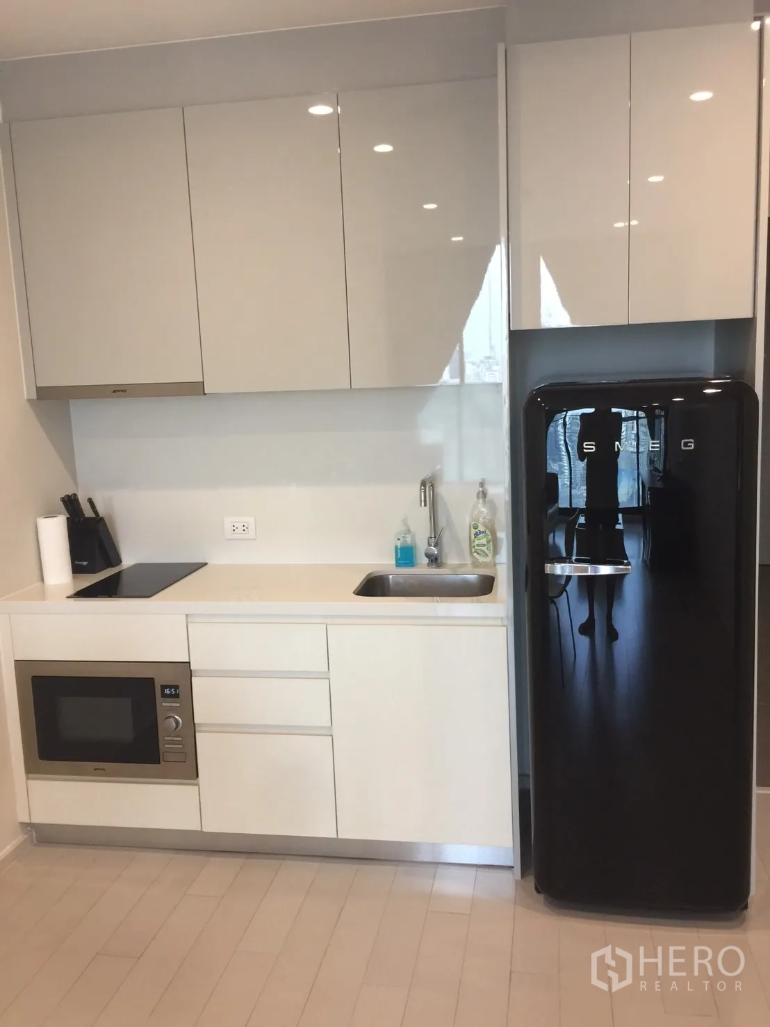 Condominium for rent in Pathum Wan, Bangkok - Modern kitchenette with glossy cabinets, cooktop, built-in microwave, and black SMEG fridge.