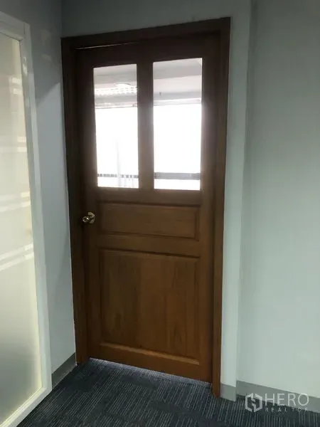 Office Space for rent - Wooden office door with glass panels next to a frosted partition in a carpeted corridor.