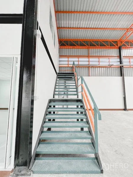 Warehouse for rent or sale in Khlong Luang, Pathum Thani - Ground-level view of steel stairs and a two-storey internal office block inside the warehouse.