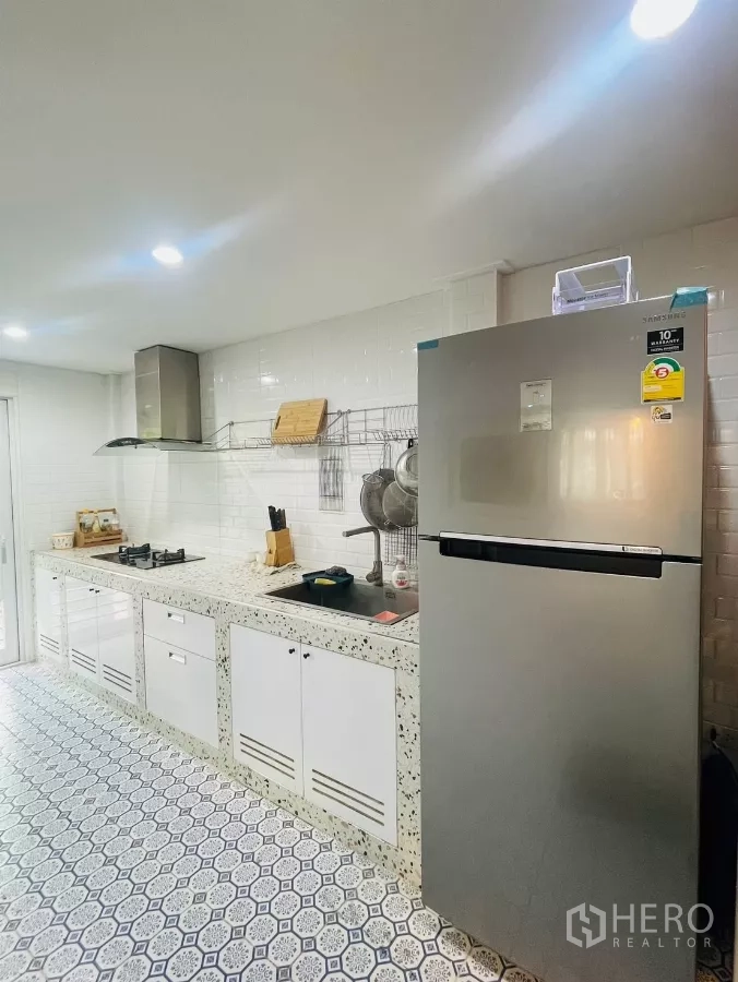 Detached House for rent in Prawet, Bangkok - Separate Thai kitchen with terrazzo countertop, gas hob, fridge and patterned tiles.