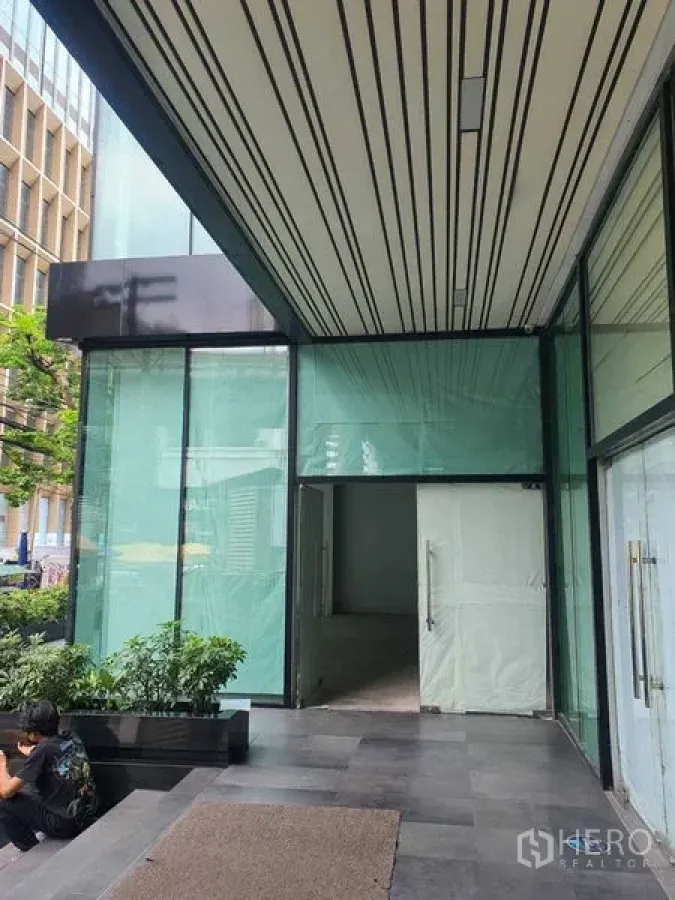 零售空间 出租在Bang Rak, Bangkok - 塔楼下方的商铺立面，高挑玻璃与门廊雨棚。