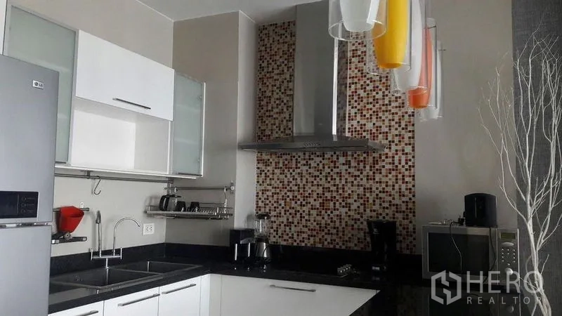 Condominium for rent in Khlong Luang, Pathum Thani - Close-up of the kitchen backsplash, stainless range hood and black stone countertop with appliances.