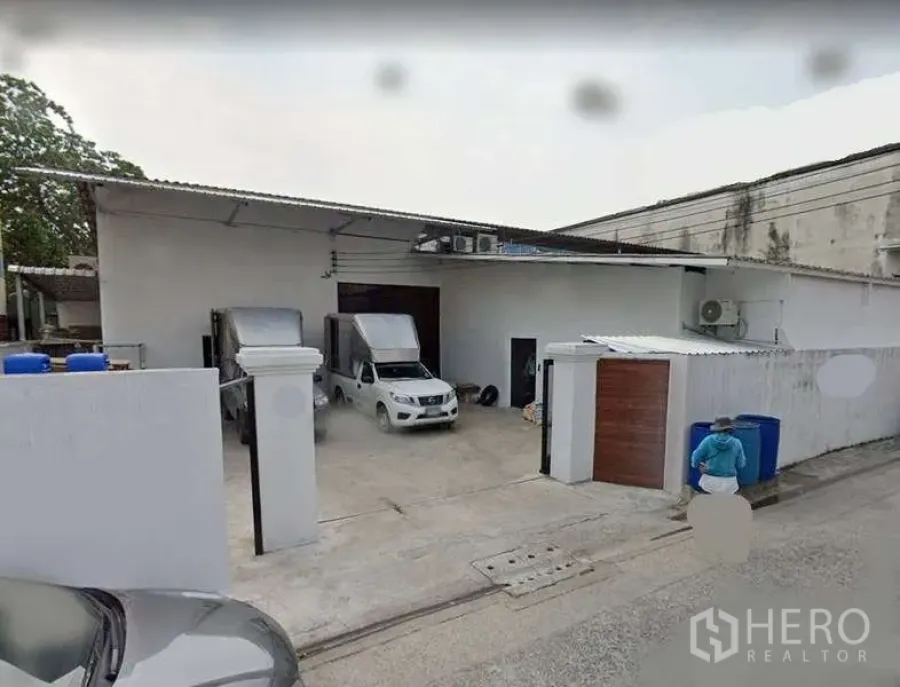คลังสินค้า ให้เช่าหรือขายในMin Buri, Bangkok - ด้านหน้าโกดังชั้นเดียวสีขาวย่านมีนบุรี พร้อมประตูม้วน ลานคอนกรีต และที่จอดรถขนส่ง
