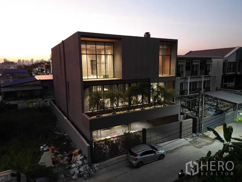 บ้าน ขายในLat Phrao, Bangkok - ด้านหน้าบ้านร่วมสมัยพร้อมทางรถเข้ามีรั้วและผนังกระจกขนาดใหญ่ยามค่ำ