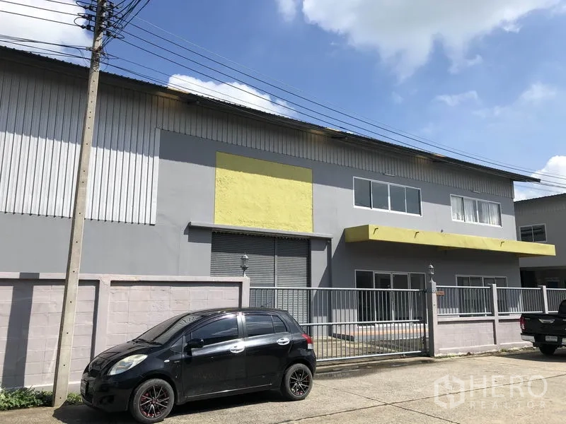 Factory for rent in Pathum Thani - Two-storey factory facade with grey walls, yellow awnings, metal gate and parking in Lat Lum Kaeo.