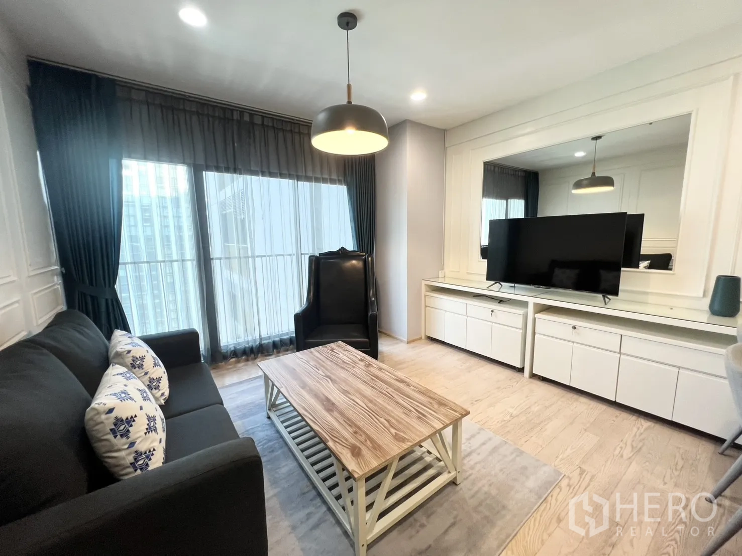 Condominium for rent in Khlong Toei, Bangkok - Bright living room with sofa, armchair, wood coffee table, built-in TV cabinet, and floor-to-ceiling windows with city outlook.