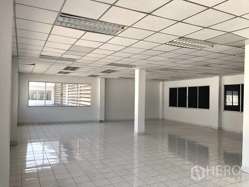 Warehouse for rent in Phra Nakhon Si Ayutthaya - Corner view of office area with white columns, fluorescent lighting and glazed windows.