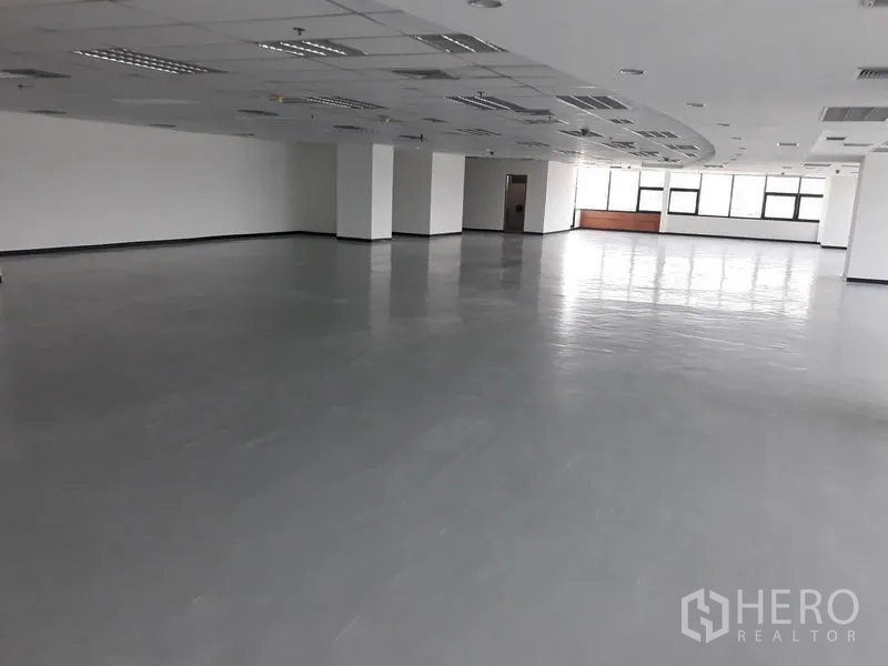 办公空间 出租在Bangkok - 宽敞开放式办公楼层，灰色抛光地面、白色立柱与吊顶照明。