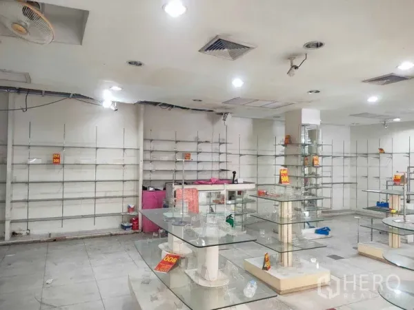 店屋 出租在Watthana, Bangkok - 宽敞的室内商铺，吊顶射灯、墙面层架与玻璃柜台，适合陈列。