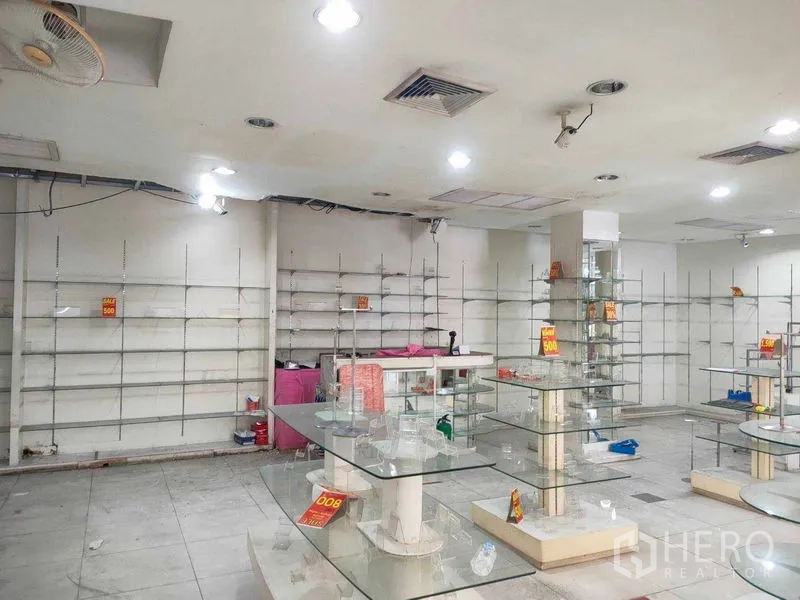 店屋 出租在Watthana, Bangkok - 宽敞的室内商铺，吊顶射灯、墙面层架与玻璃柜台，适合陈列。