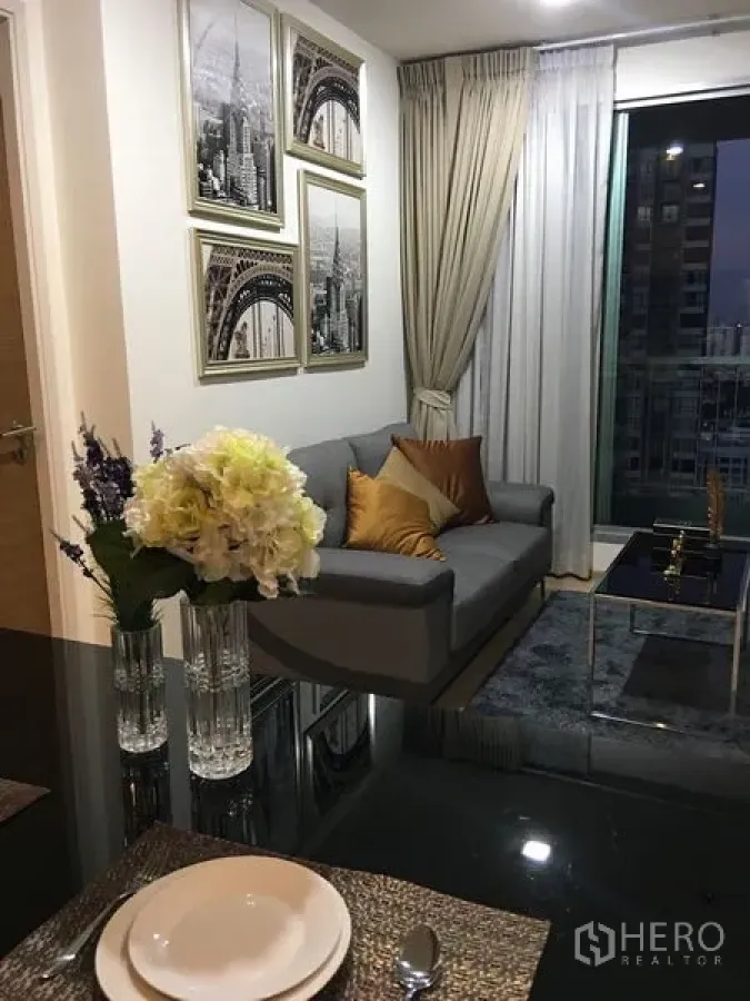 Condominium for rent in Khlong Toei, Bangkok - Modern living room with grey sofa, framed art, rug and a city‑view window in a Sukhumvit condo near BTS On Nut.