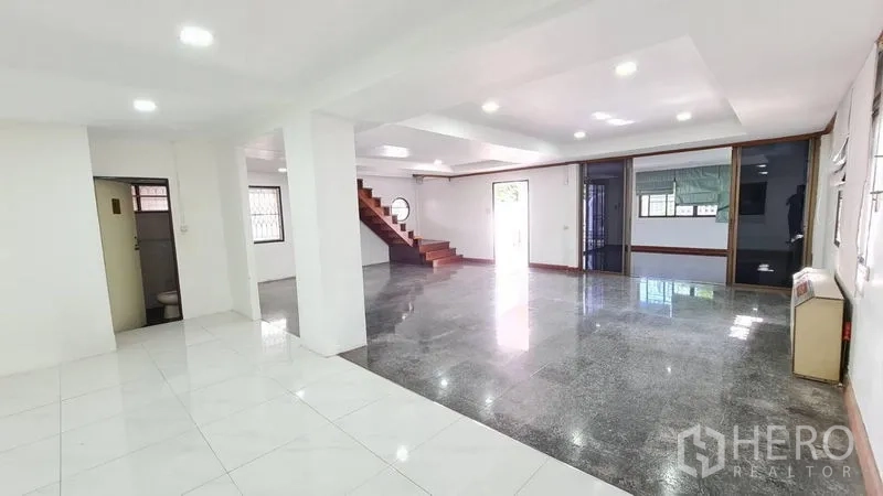 Detached House for rent in Lat Phrao, Bangkok - Bright open-plan living area with recessed lighting, mixed tile flooring and wooden staircase.