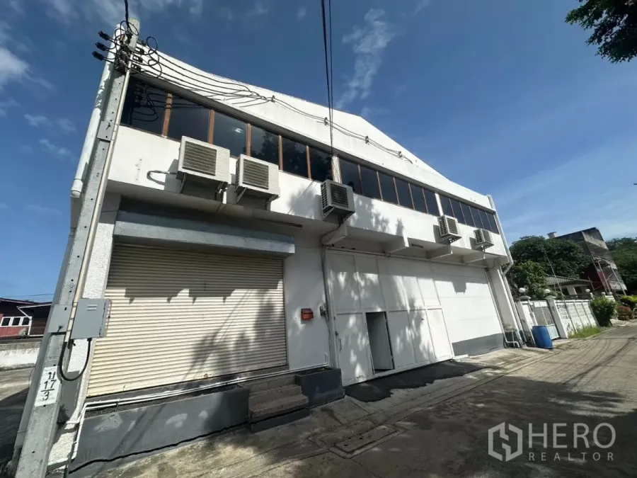 Warehouse for rent in Bang Na, Bangkok - Street-facing two-storey warehouse exterior with roller shutters and multiple AC units in Bang Na.