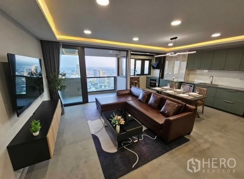 Condominium for rent or sale - Open-plan living room with leather sectional, TV wall and balcony city view.