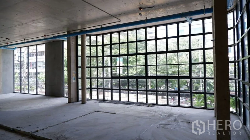 Retail Space for rent in Watthana, Bangkok - Wide corner facade featuring panoramic grid glass framing views of the street and trees.