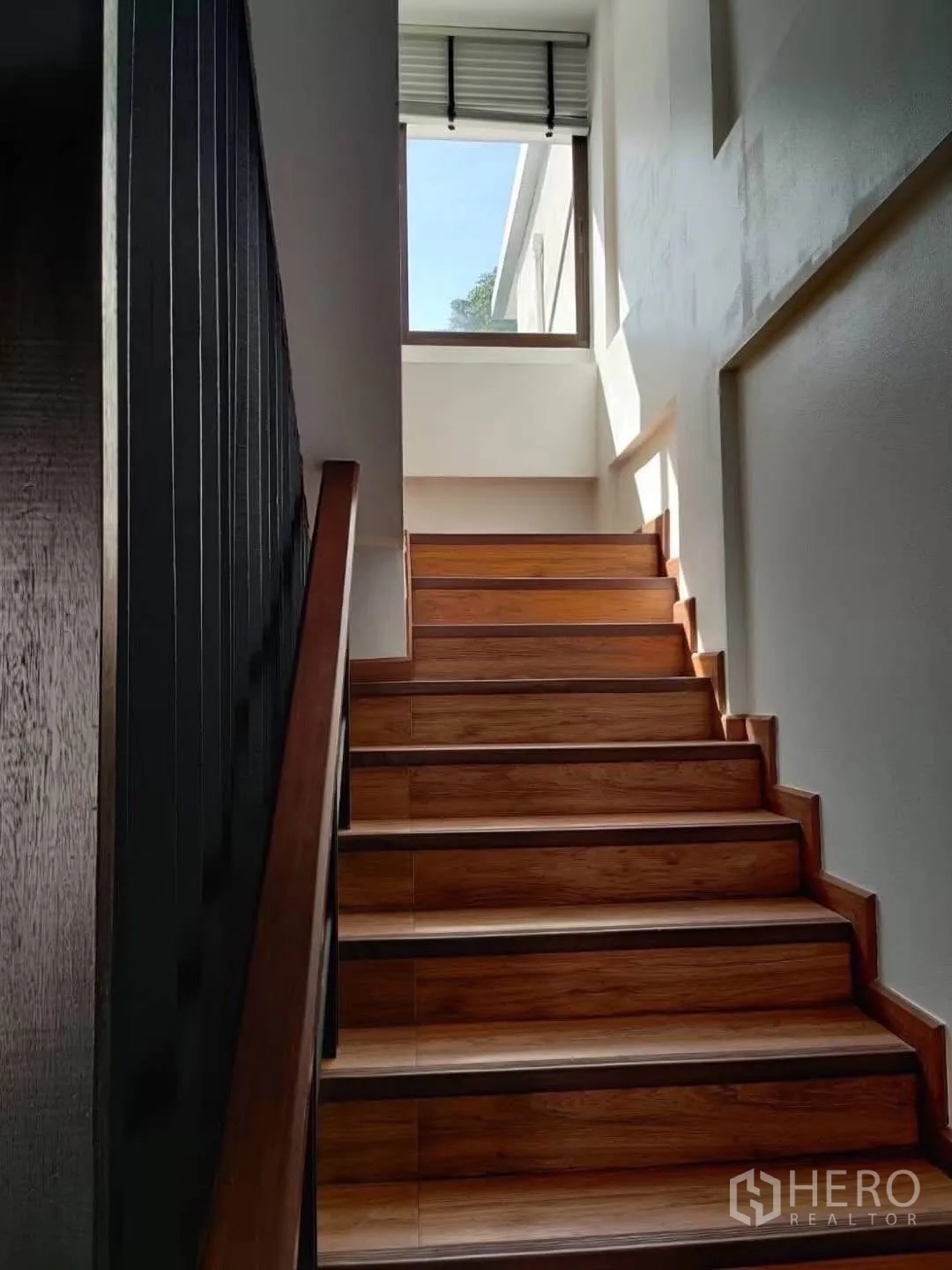 Townhouse for rent in Suan Luang, Bangkok - Sunlit wooden staircase rising to the upper floor with a side window.