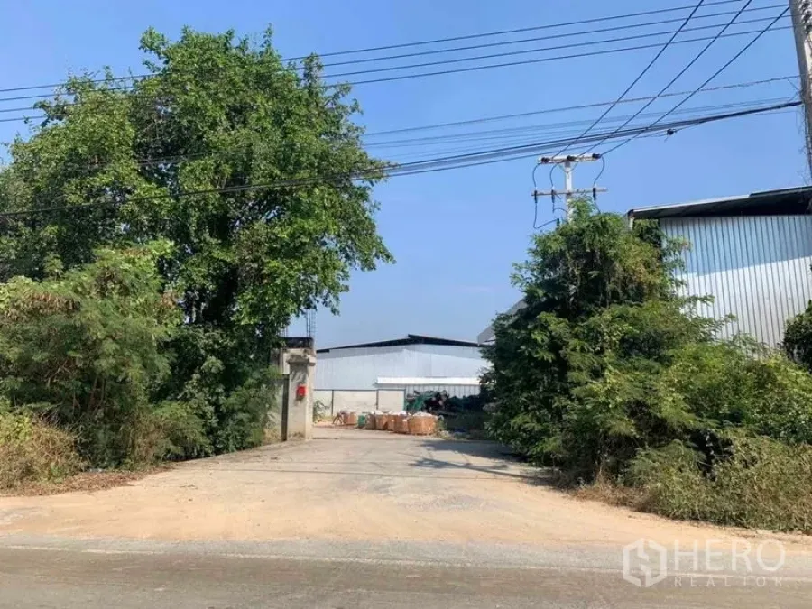 Factory for rent in Nakhon Pathom - Entrance driveway from the main road with power lines leading to the industrial site.