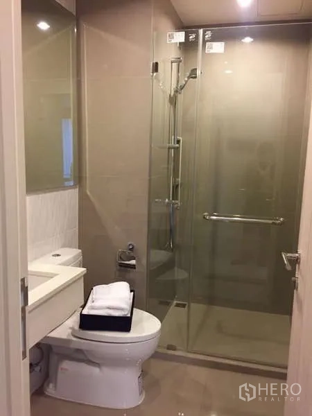 Condominium for rent in Khlong Toei, Bangkok - Compact bathroom with toilet and clear glass shower enclosure.