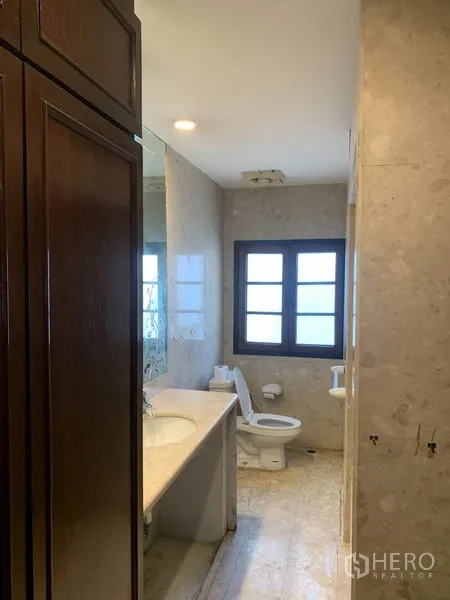 Townhouse for rent or sale in Phra Khanong, Bangkok - Bathroom with marble tiles, vanity countertop, large mirror and a window.