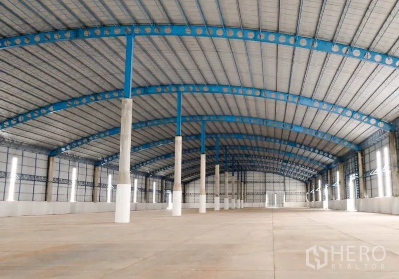 Warehouse for rent in Ban Pho, Chachoengsao - Vast clear-span warehouse interior with blue steel trusses and smooth concrete floor.