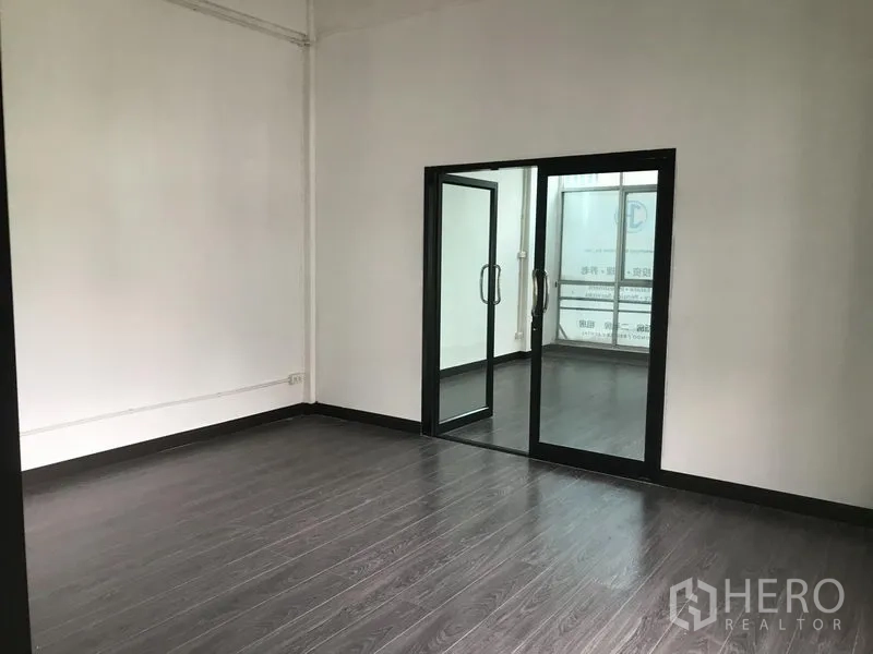 Shophouse for rent in Watthana, Bangkok - Spacious workspace with dark floors and sliding glass doors to an adjoining room.