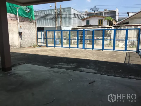 Warehouse for rent in Bueng Kum, Bangkok - Gated concrete yard with blue sliding fence offering easy truck access and on-site parking.
