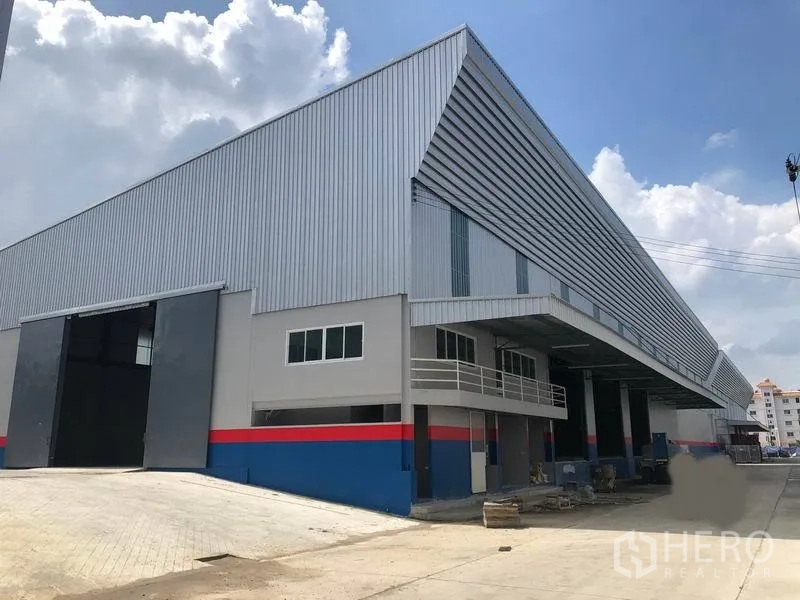 Warehouse for rent in Bang Phli, Samut Prakan - Modern metal-clad warehouse exterior with a covered, raised loading dock and wide truck driveway in an industrial estate.