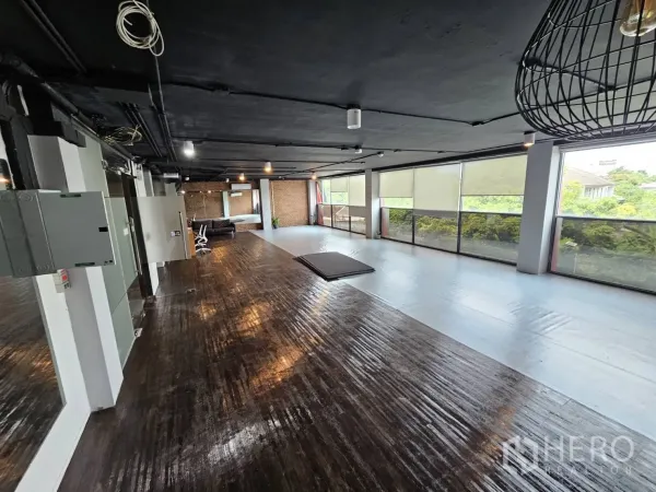 Office Space for rent in Watthana, Bangkok - Spacious workspace with a run of windows facing greenery, dark wood floors and an industrial black ceiling.