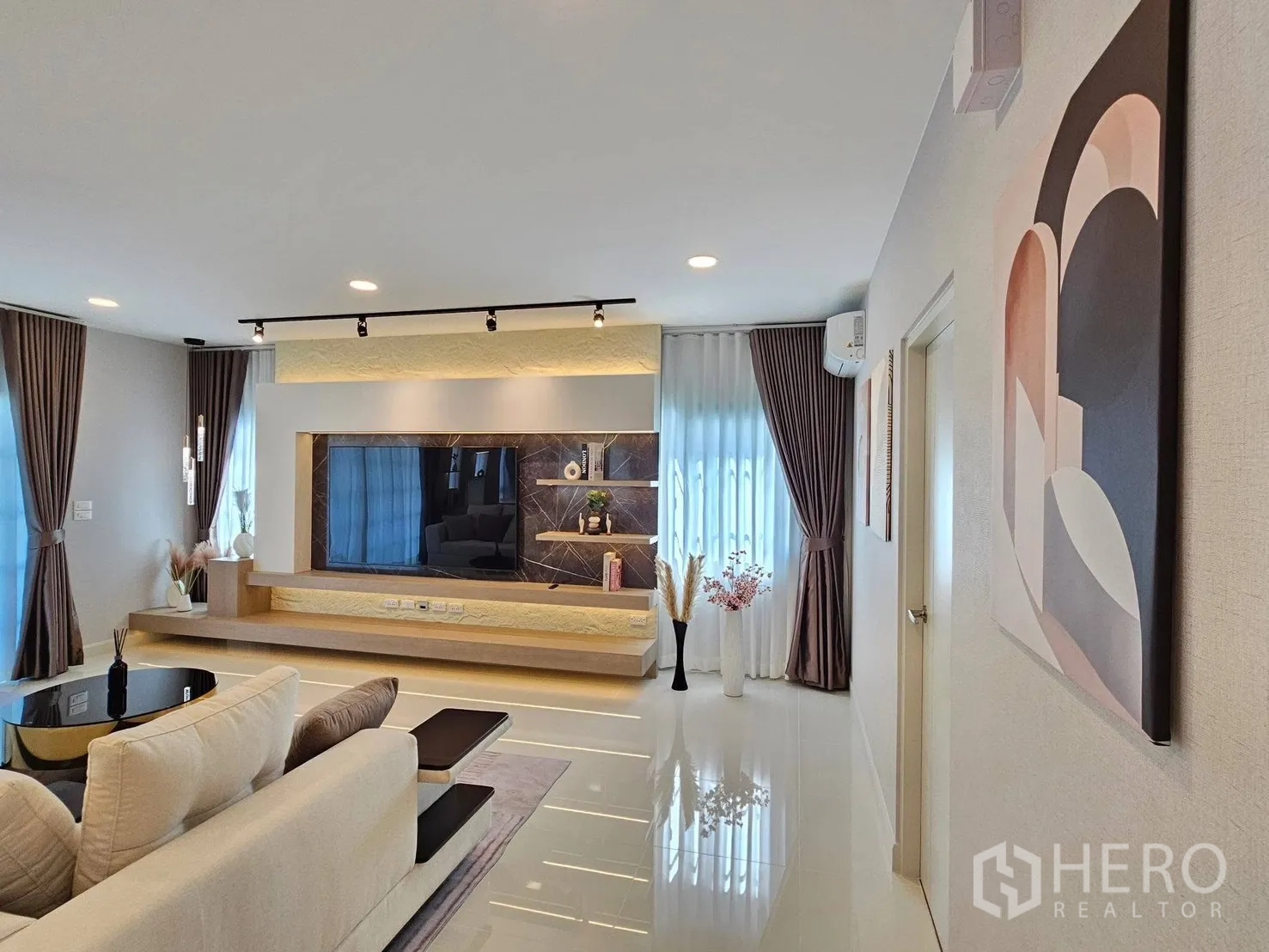 Detached House for rent or sale in Bang Phli, Samut Prakan - Contemporary living room with L‑shaped sofa, feature TV wall and full‑height curtains.