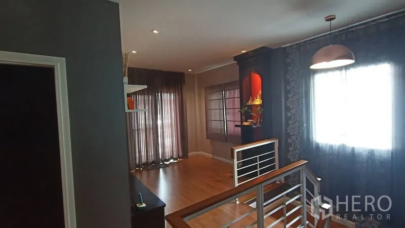 Detached House for sale in Prawet, Bangkok - Upstairs landing with pendant light, railing and floor-to-ceiling curtains.