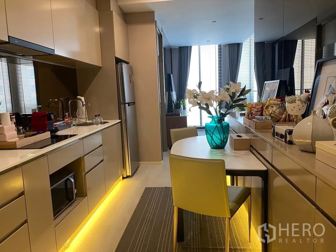 Condominium for rent in Pathum Wan, Bangkok - Galley kitchen with integrated appliances, breakfast table, and reflective mirror wall.