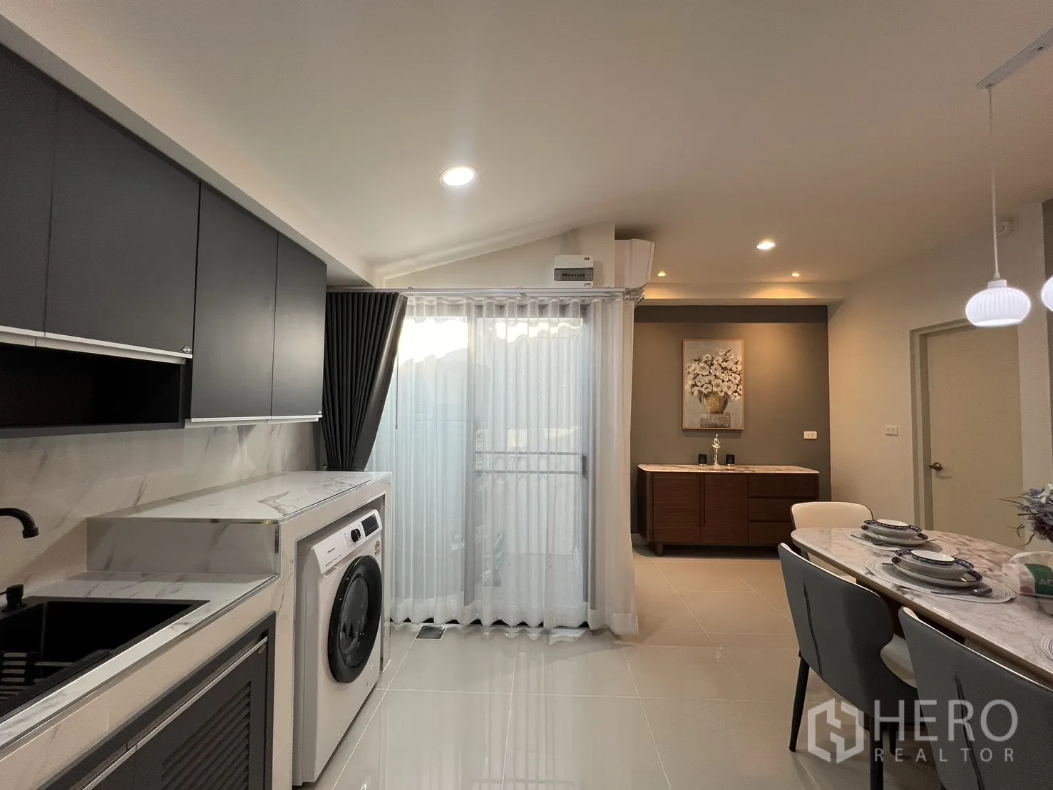 Townhouse for rent in Bang Phli, Samut Prakan - Modern kitchen with washing machine, black sink and sliding glass door with sheer curtains.