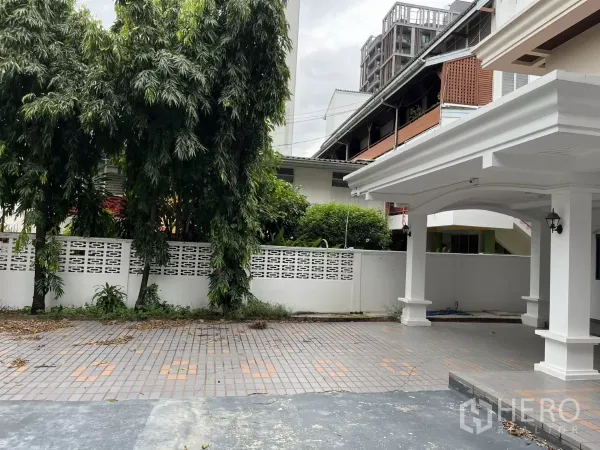 独立式住宅 出租在Watthana, Bangkok - 前院空间宽敞，铺砖露台、白色围墙与绿化，毗邻车棚。