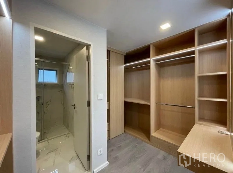 Detached House for rent in Prawet, Bangkok - Walk-in closet with custom wood cabinetry beside a bathroom with glass-enclosed shower.