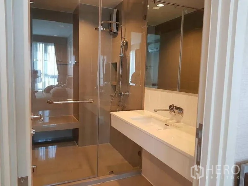 Condominium for rent or sale in Khlong Toei, Bangkok - Contemporary bathroom with glass-enclosed shower, bench and long vanity.