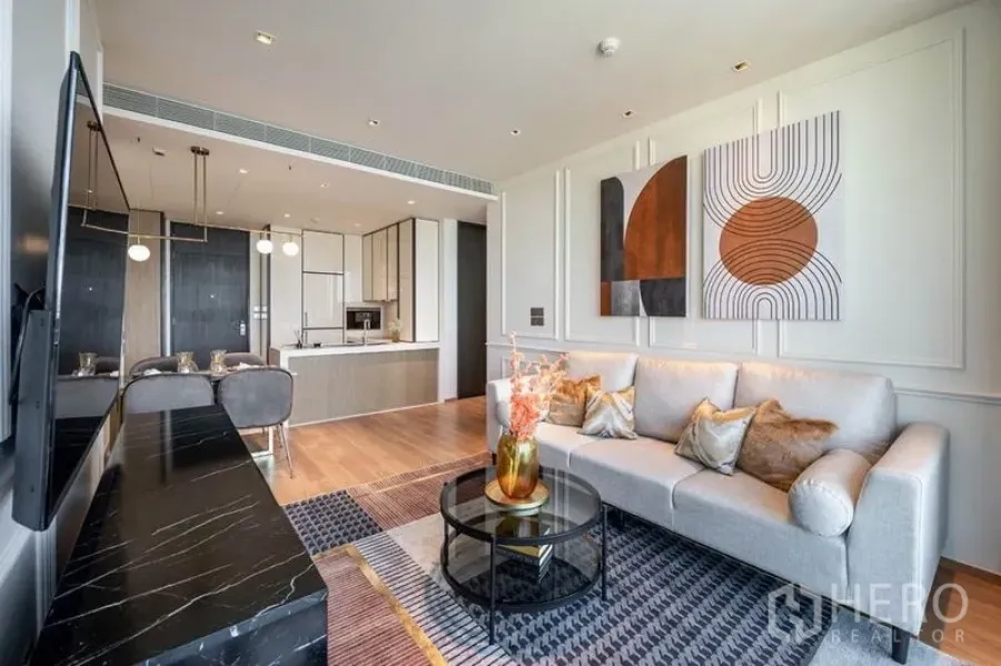 Condominium for rent in Khlong Toei, Bangkok - Bright living room with sofa, wall art and an open-plan kitchen in a modern Bangkok condo.